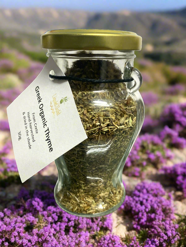 Cretan organic thyme in glass amphora jar, 30g, against backdrop of wild thyme bushes on the Cretan mountains