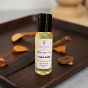 Bottle of Liquid Gold Sandalwood shaving oil on a wooden tray with sandalwood pieces.